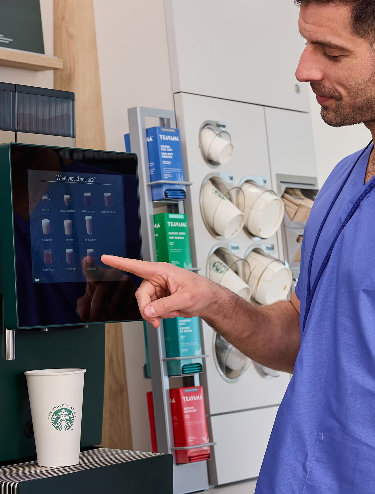 Zorgverlener die een drankje selecteert bij de We Proudly Serve Starbucks koffiemachine