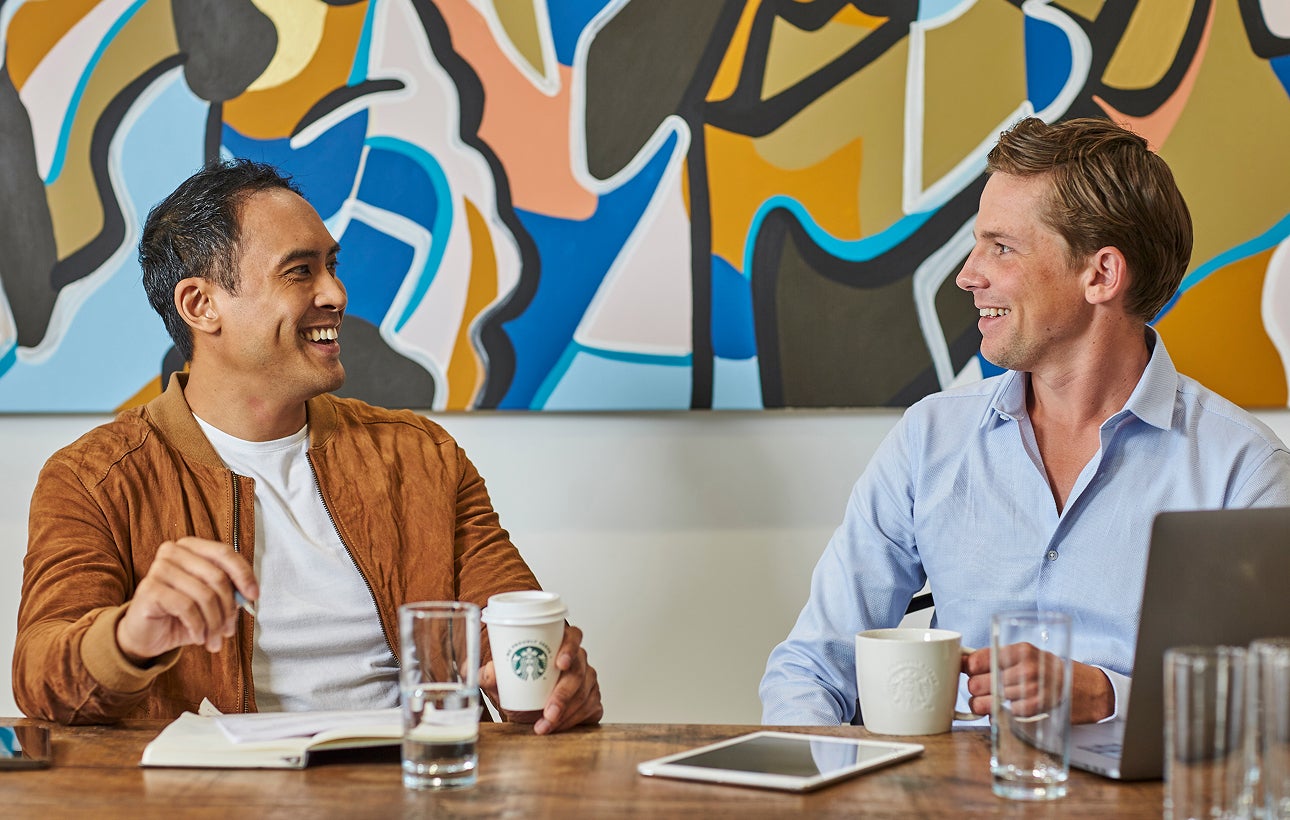Mannen zitten aan een tafel en houden We Proudly Serve Starbucks koffie vast