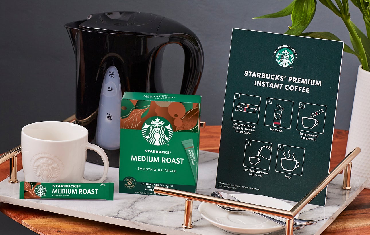 Een tafelblad met een We Proudly Serve Starbucks mok, Starbucks Premium oploskoffie en bereidingsinstructies