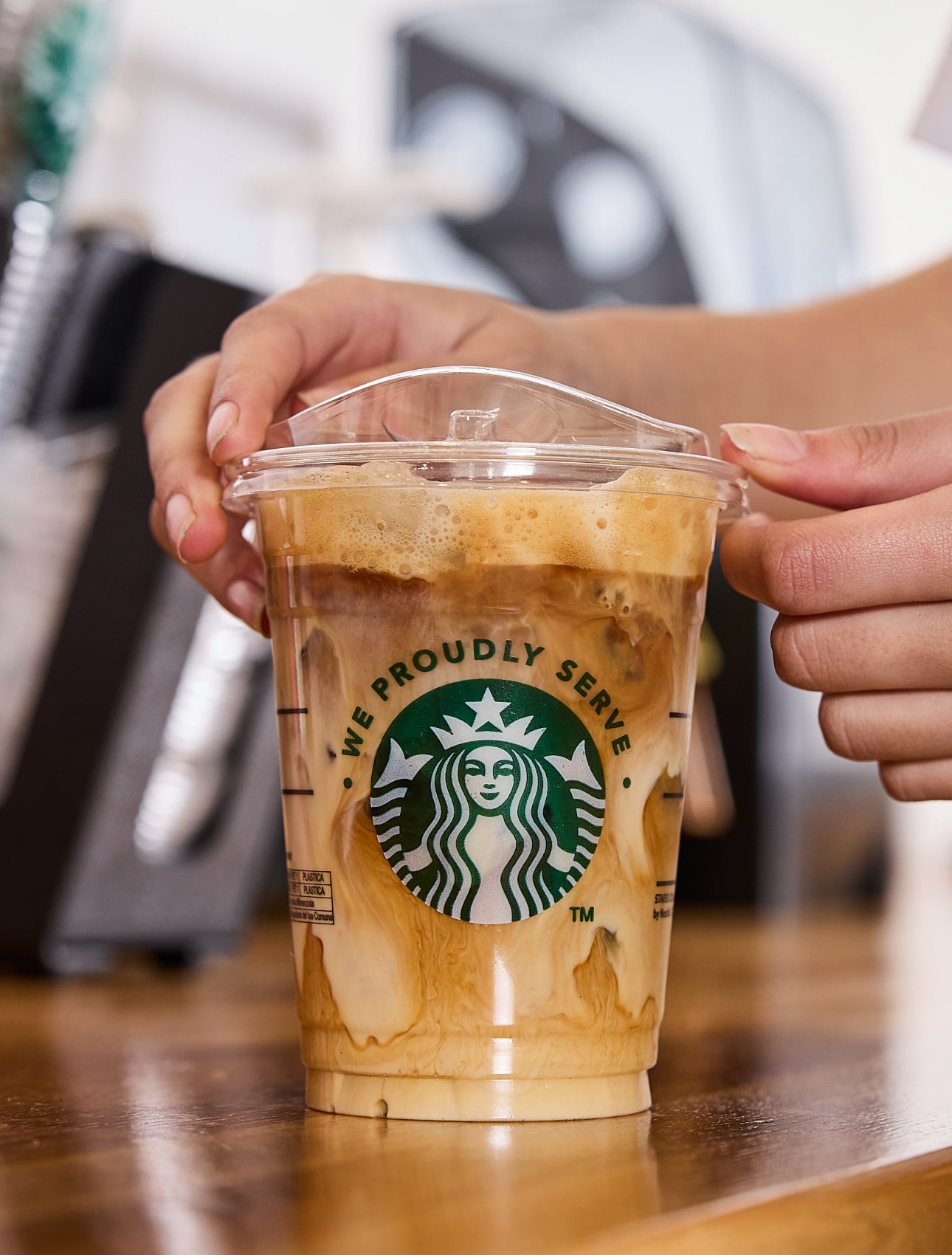 Een barista plaatst een deksel op een We Proudly Serve Starbucks beker met ijskoffie, versierd met toefjes room en koffie