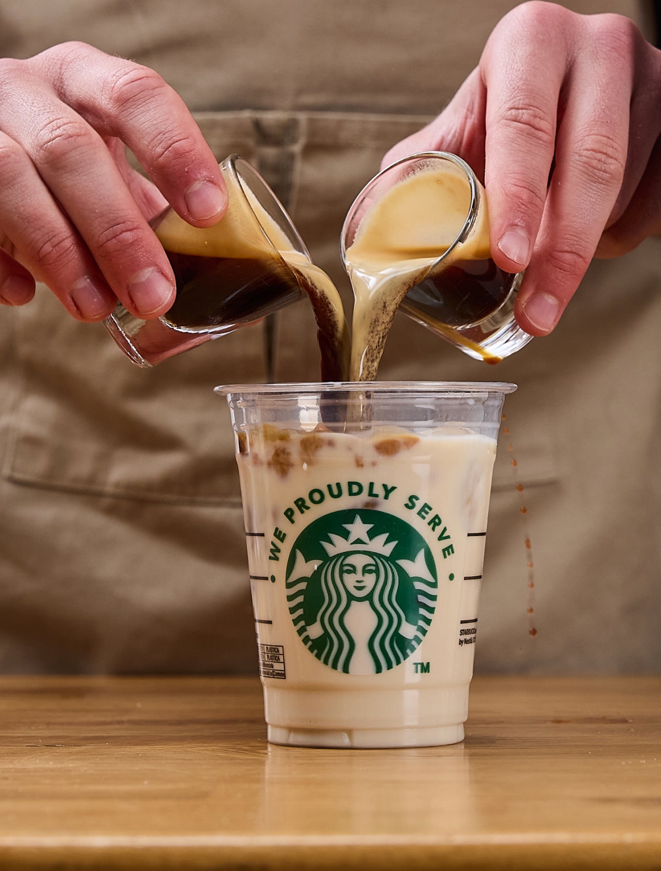 Een barista schenkt twee espressoshots tegelijk in een We Proudly Serve Starbucks beker gevuld met ijs en melk