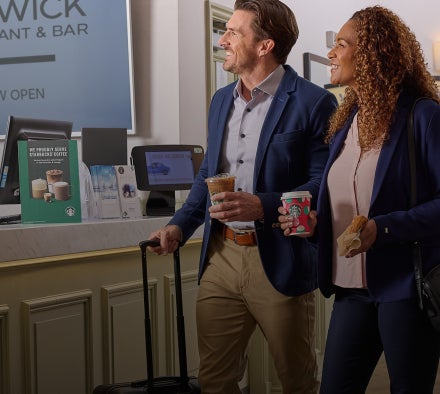 Een man en een vrouw lopen door de lobby van een hotel met Starbucks dranken in hun hand