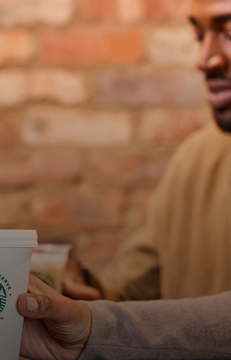 Een persoon houdt een We Proudly Serve Starbucks beker vast voor een wazige bakstenen achtergrond