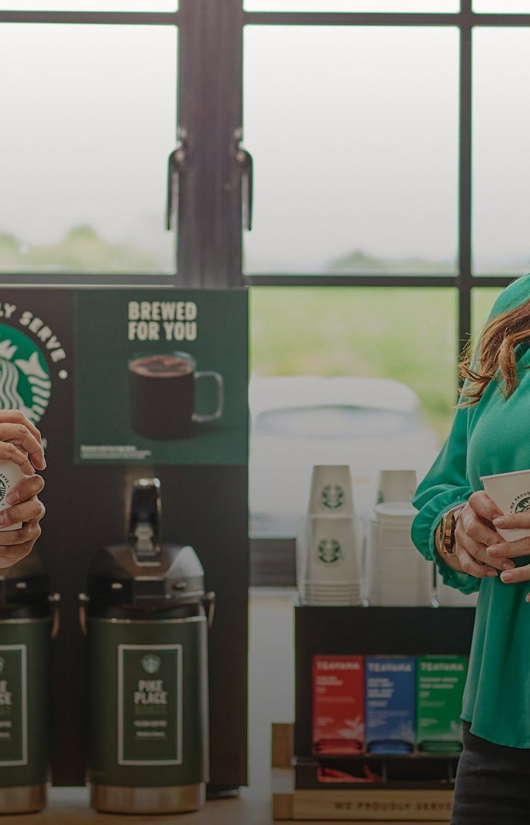 Twee mensen staan te praten terwijl ze We Proudly Serve Starbucks bekers vasthouden, voor filterkoffieautomaten.