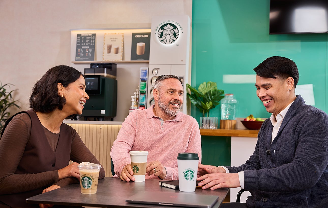 Des collègues assis ensemble avec des tasses We Proudly Serve Starbucks et une machine à café professionnelle en libre-servic