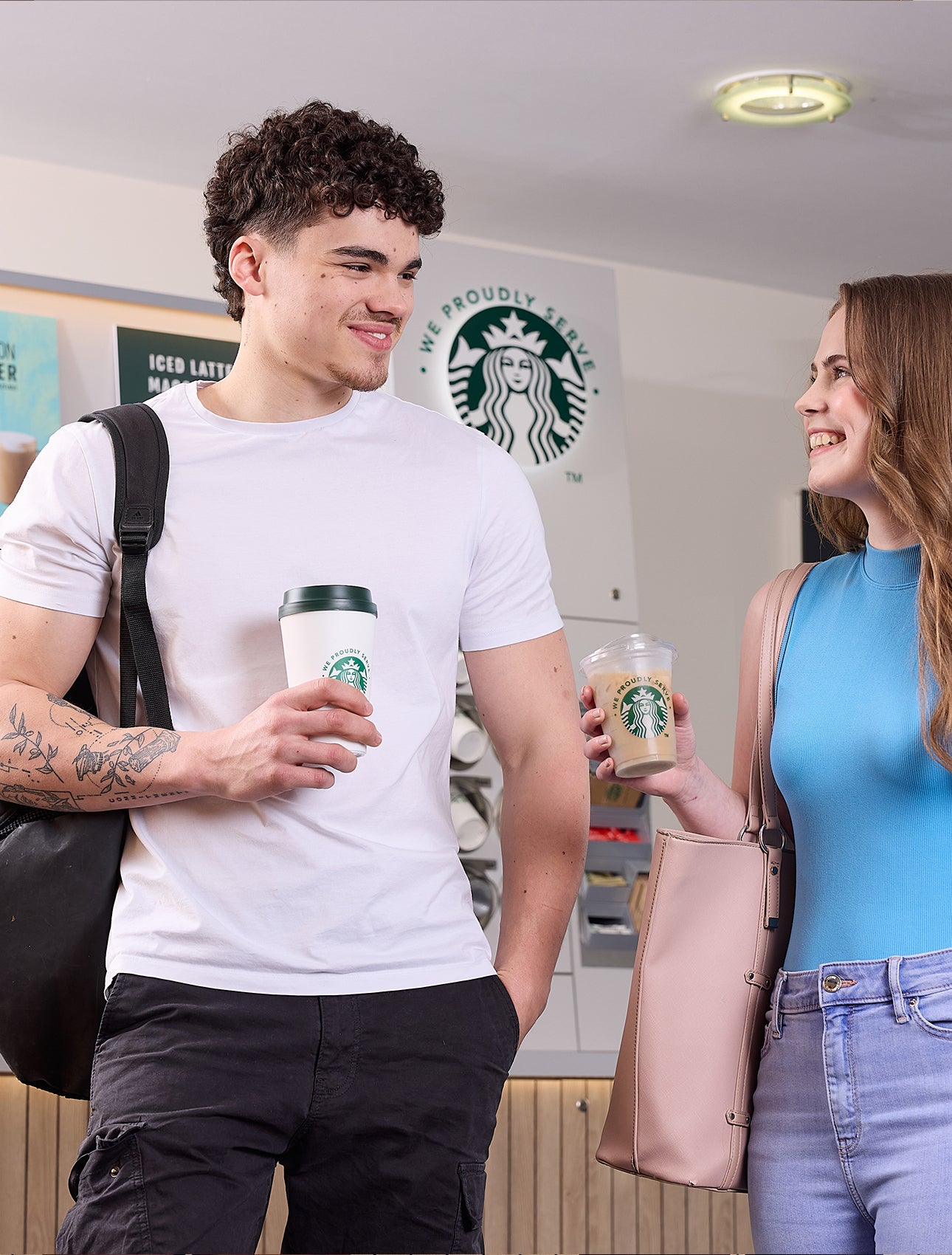 Un homme et une femme debout devant une machine à café autonome en libre-service We Proudly Serve Starbucks