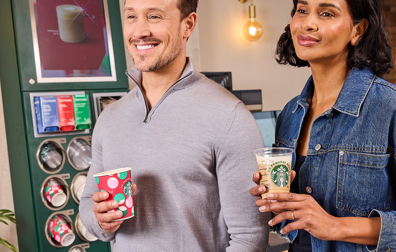 Un homme tenant une tasse de café festive We Proudly Serve Starbucks et une femme tenant un café glacé