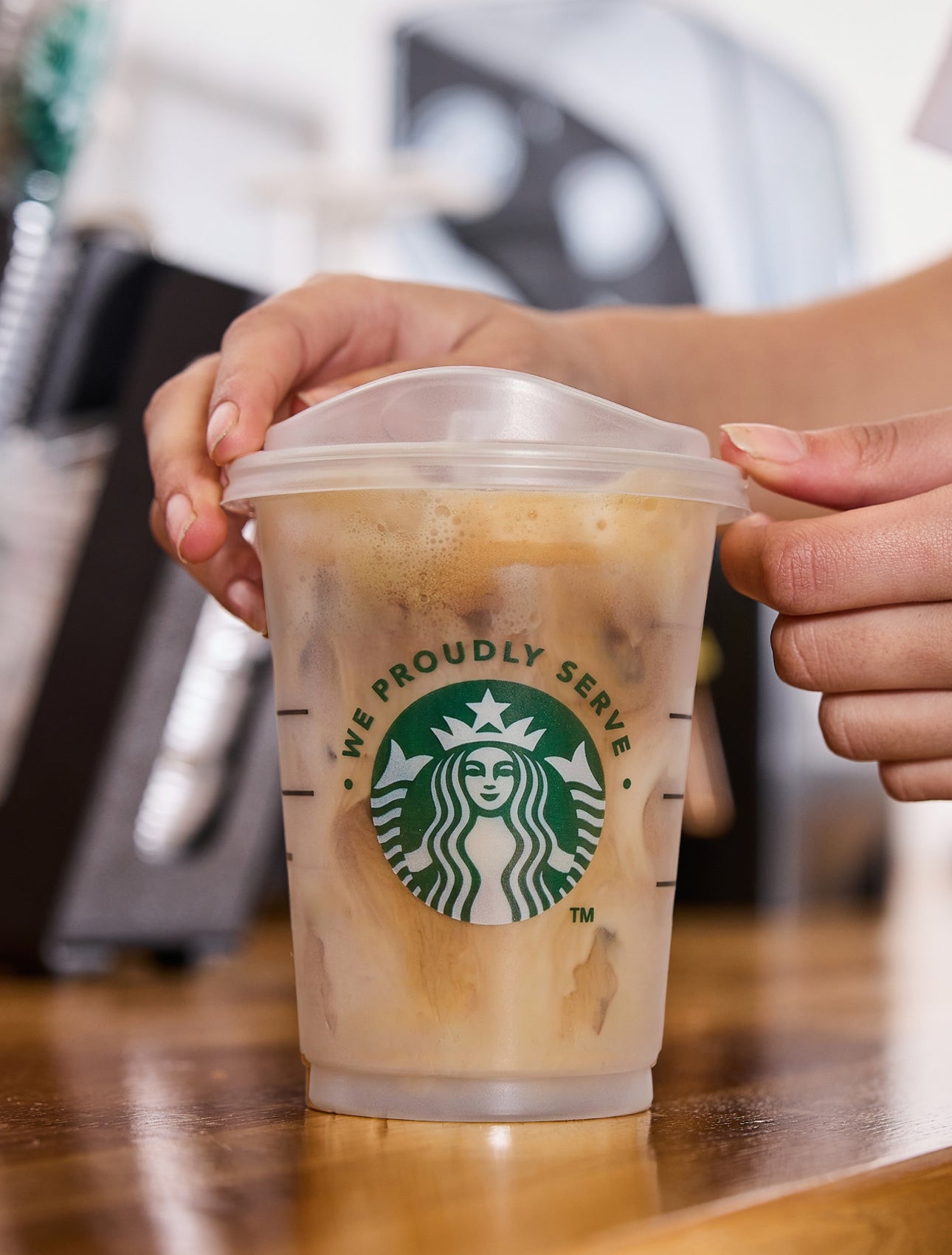 Un barista servant un verre We Proudly Serve Starbucks rempli de café glacé, dévoilant des couches de café et de crème