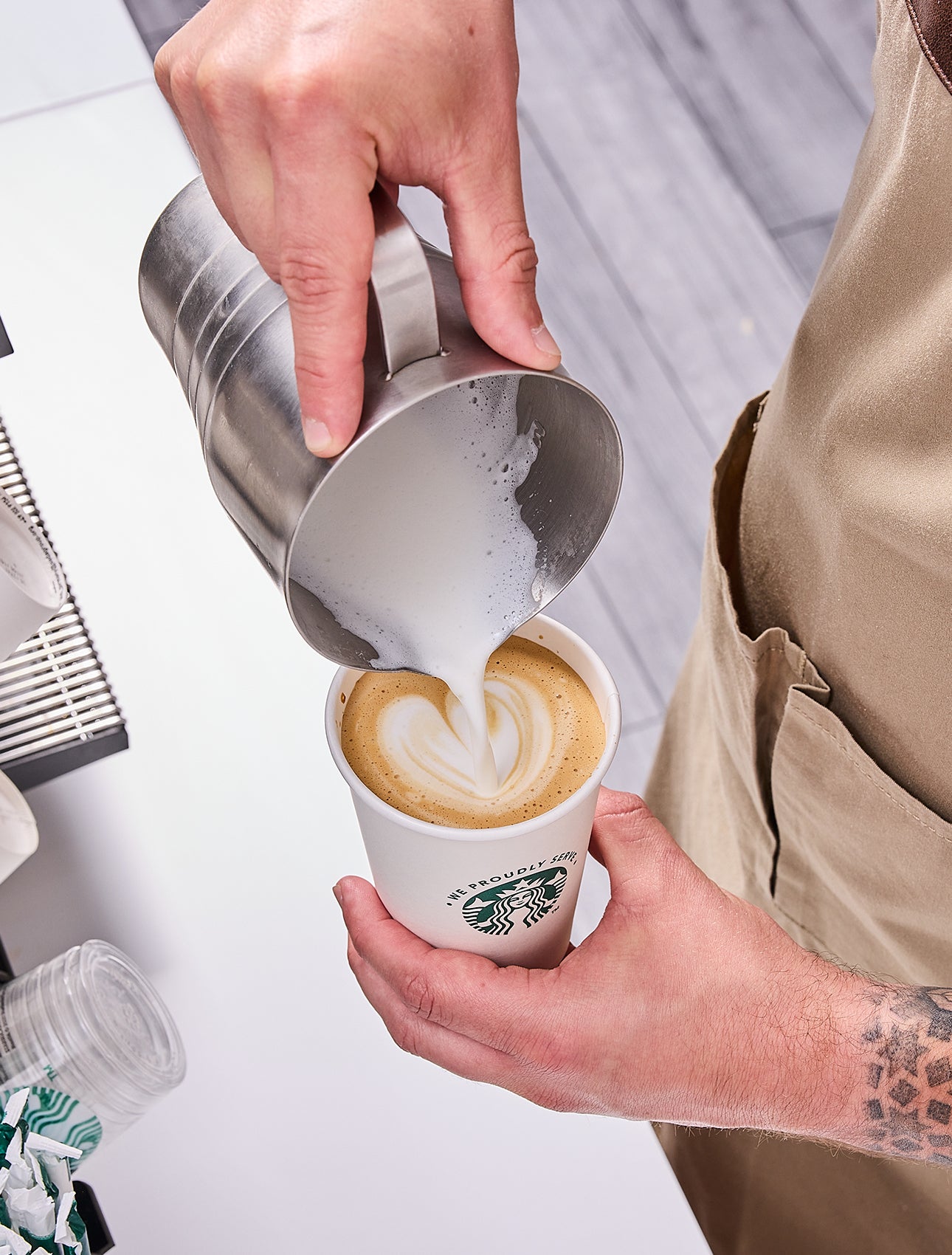 Un barista servant un verre We Proudly Serve Starbucks rempli de café glacé, dévoilant des couches de café et de crème