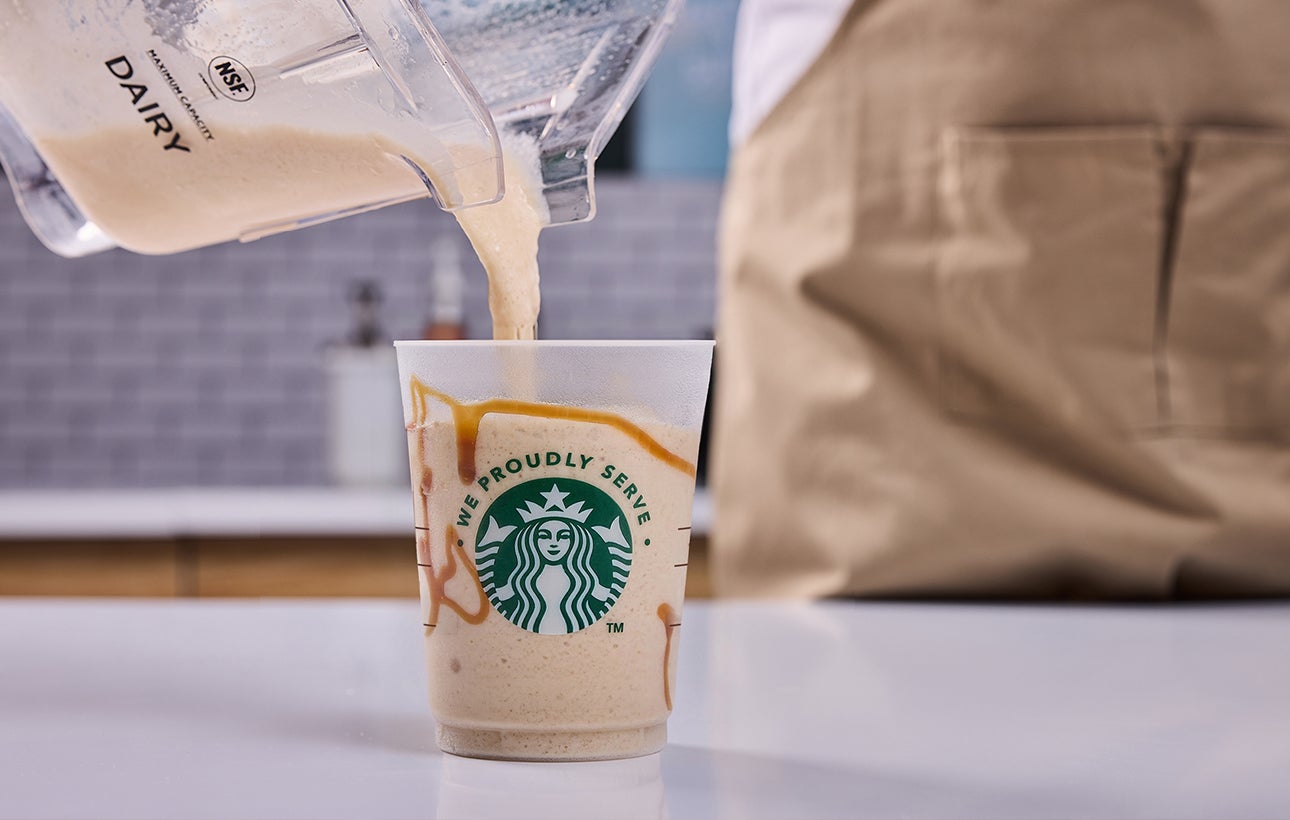 Une boisson We Proudly Serve Starbucks nappée de crème fouettée, avec un filet de chocolat ajouté par un barista.