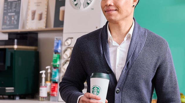 Collaborateur souriant avec café We Proudly Serve Starbucks et un ordinateur portable devant une machine à café libre-service