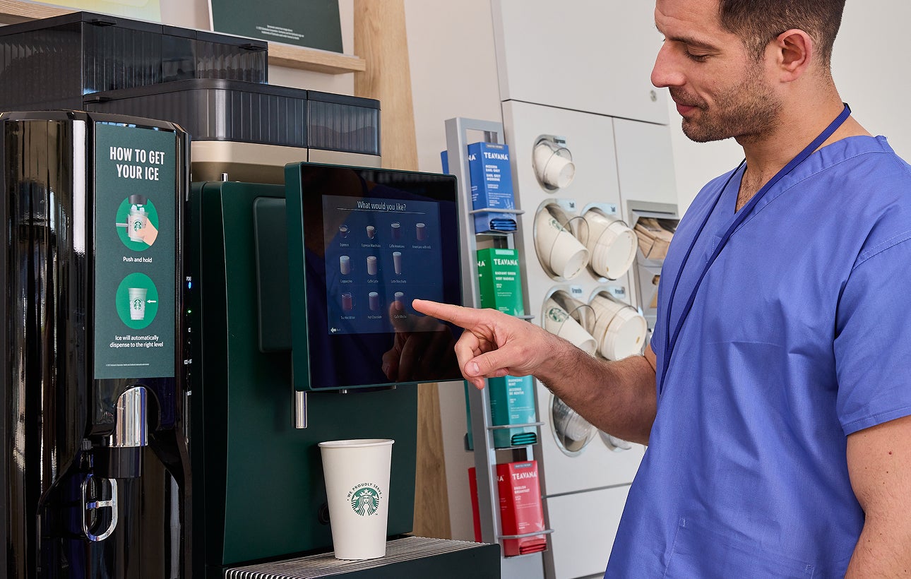 Healthcare professional selecting a drink on self-serve We Proudly Serve Starbucks coffee machine