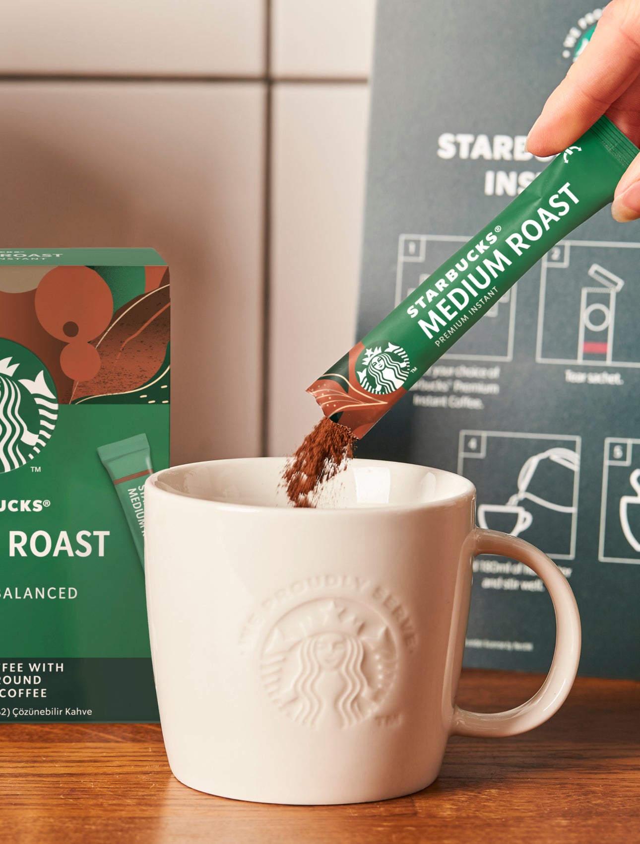 A Starbucks Premium Instant Medium Roast coffee sachet being poured into a ceramic We Proudly Serve Starbucks mug