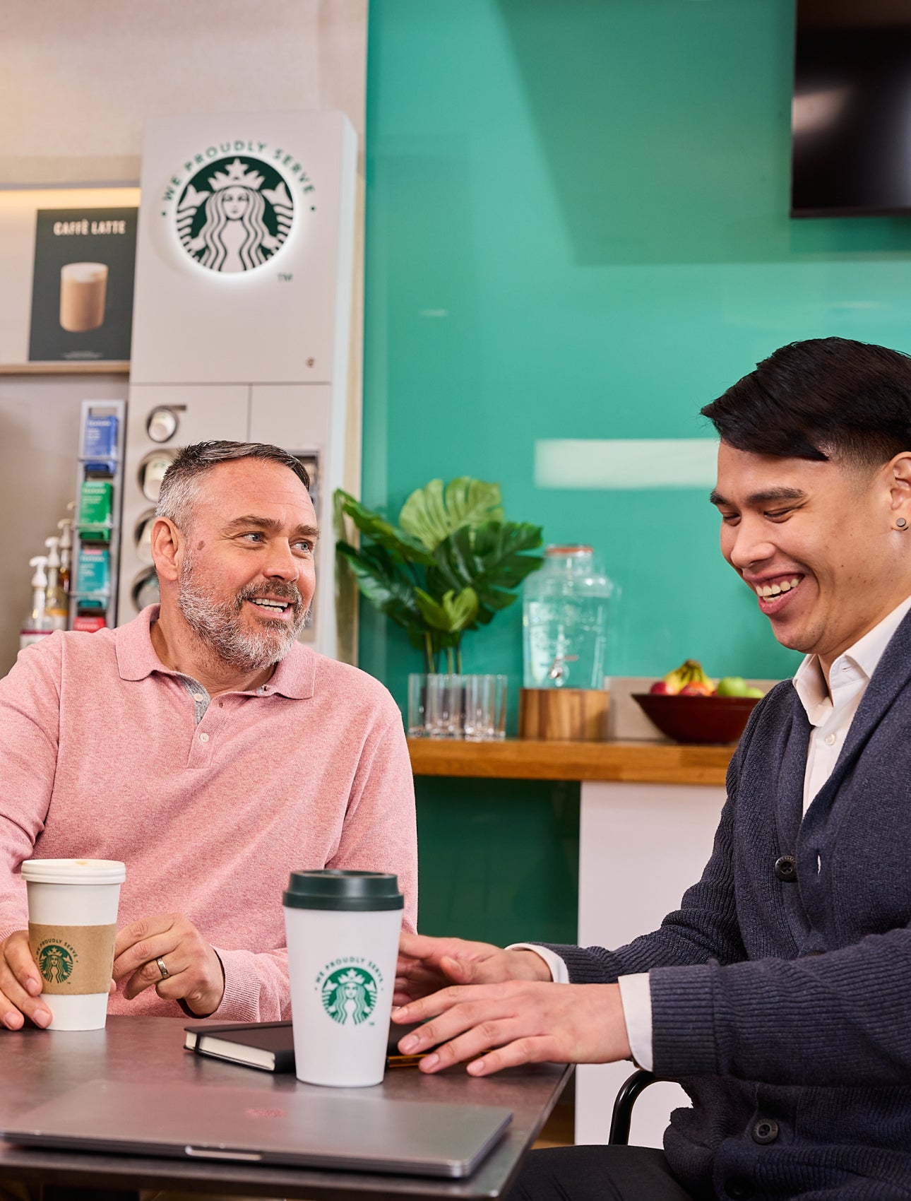 Colleagues sitting together with We Proudly Serve Starbucks cups and a self-serve coffee machine in the background