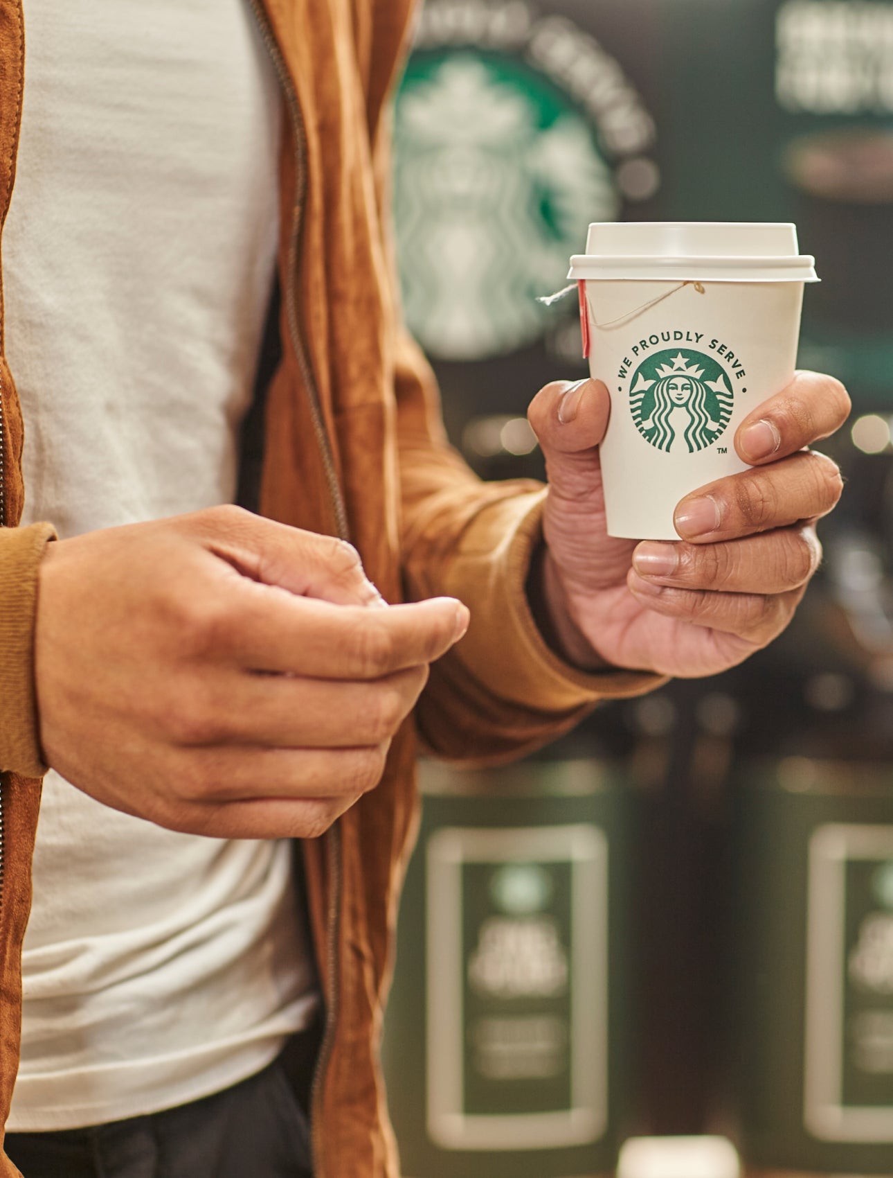 A person holding a cup of tea in a We Proudly Serve Starbucks takeaway cup