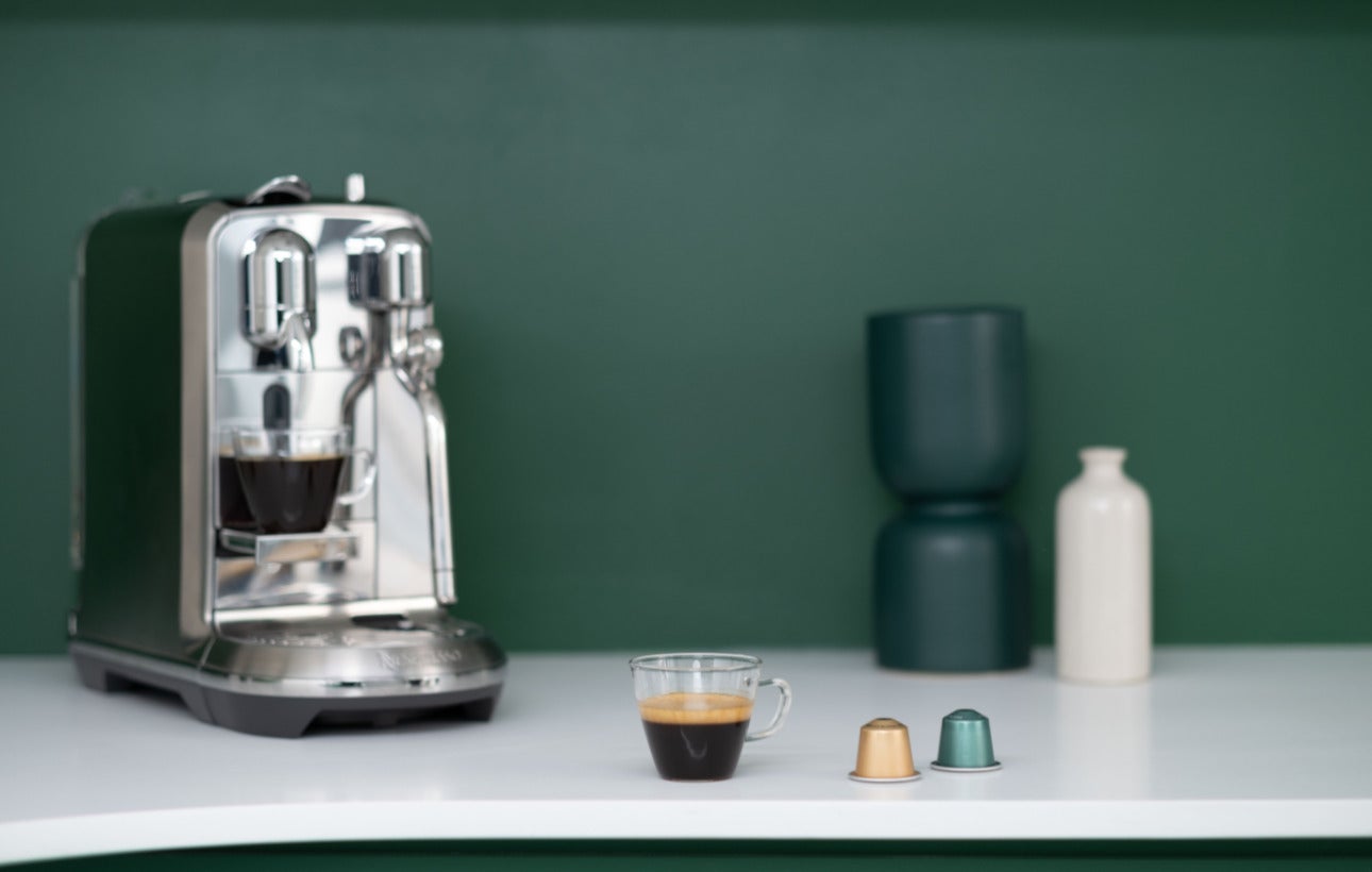 Espresso and We Proudly Serve Starbucks coffee capsules in front of Nespresso machine on counter top