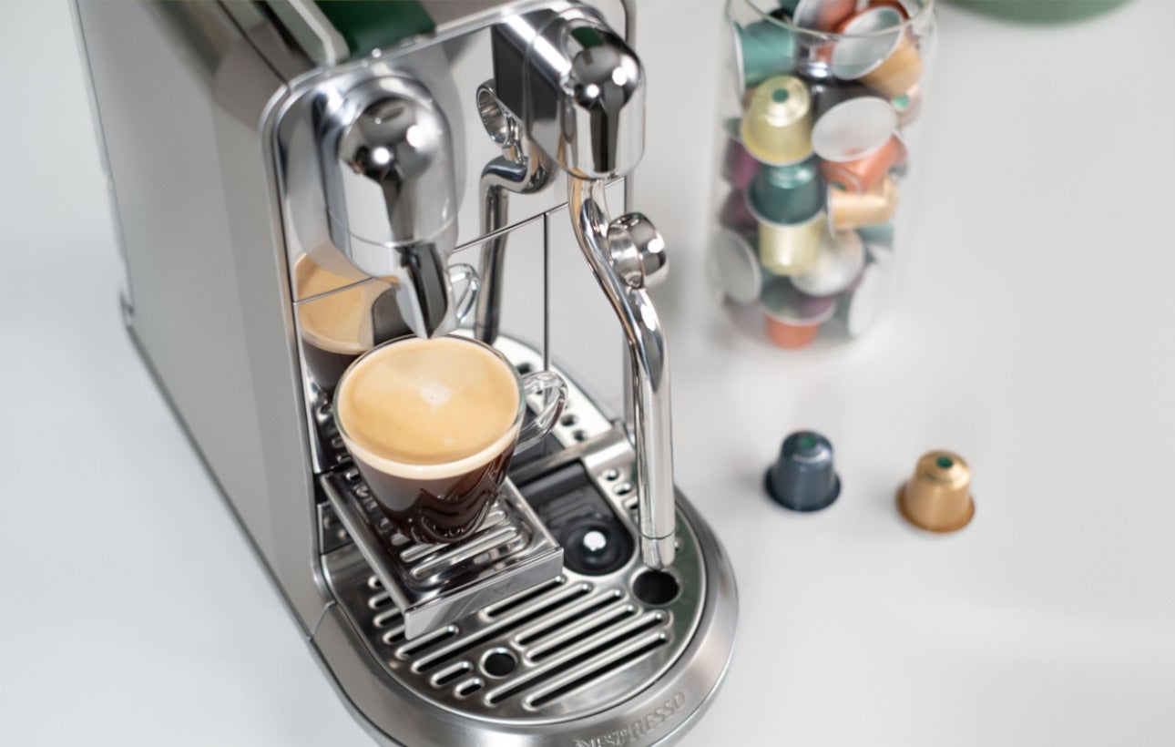 Nespresso machine with coffee and We Proudly Serve Starbucks capsules in the back