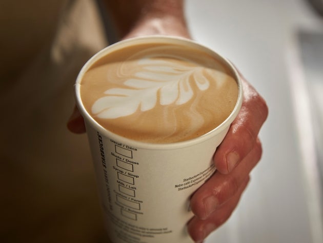 A hand holding a cup of We Proudly Serve Starbucks coffee with latte art on top