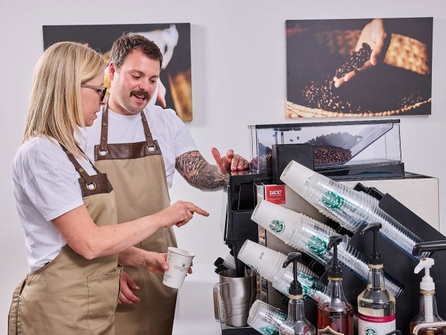 Two baristas wearing aprons, operating a Starbucks approved coffee machine
