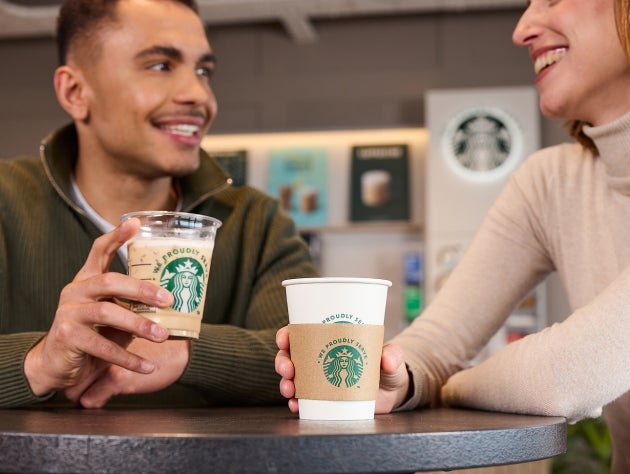 Two people holding We Proudly Serve Starbucks beverages in a café
