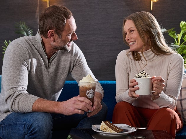 A man and woman sitting together enjoying hot and cold Starbucks beverages