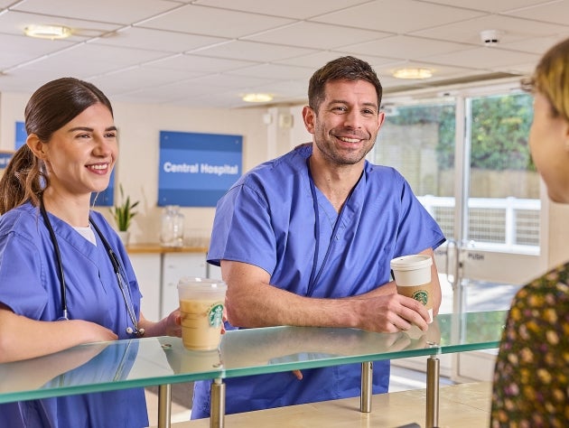 Two healthcare professionals in blue scrubs holding Starbucks drinks at a counter