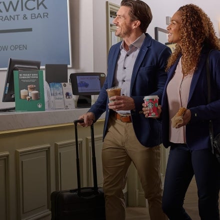 A man and woman walk through a hotel lobby holding Starbucks beverages