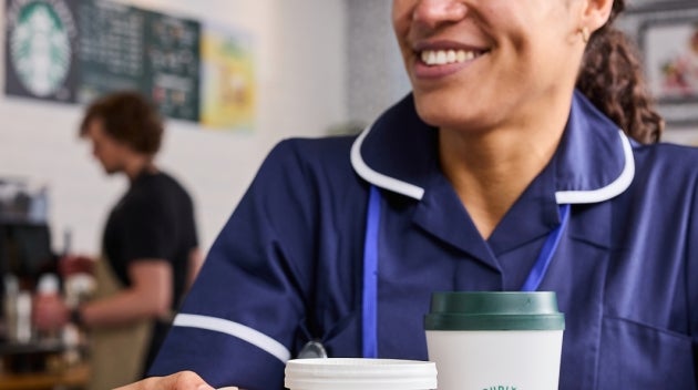 Healthcare professionals sitting together in a hospital café, holding We Proudly Serve Starbucks drinks