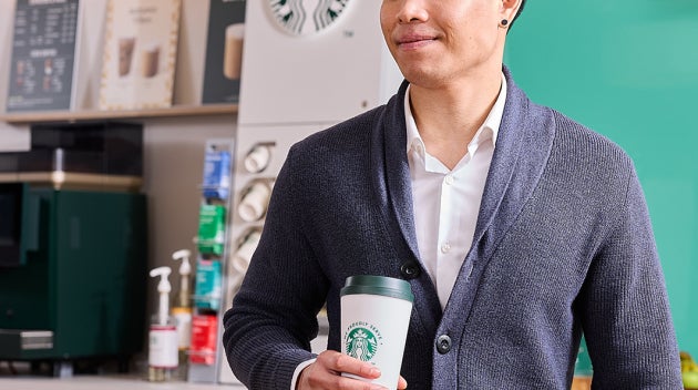 Smiling employee with We Proudly Serve Starbucks coffee and laptop in his hands in front of a self-serve coffee machine