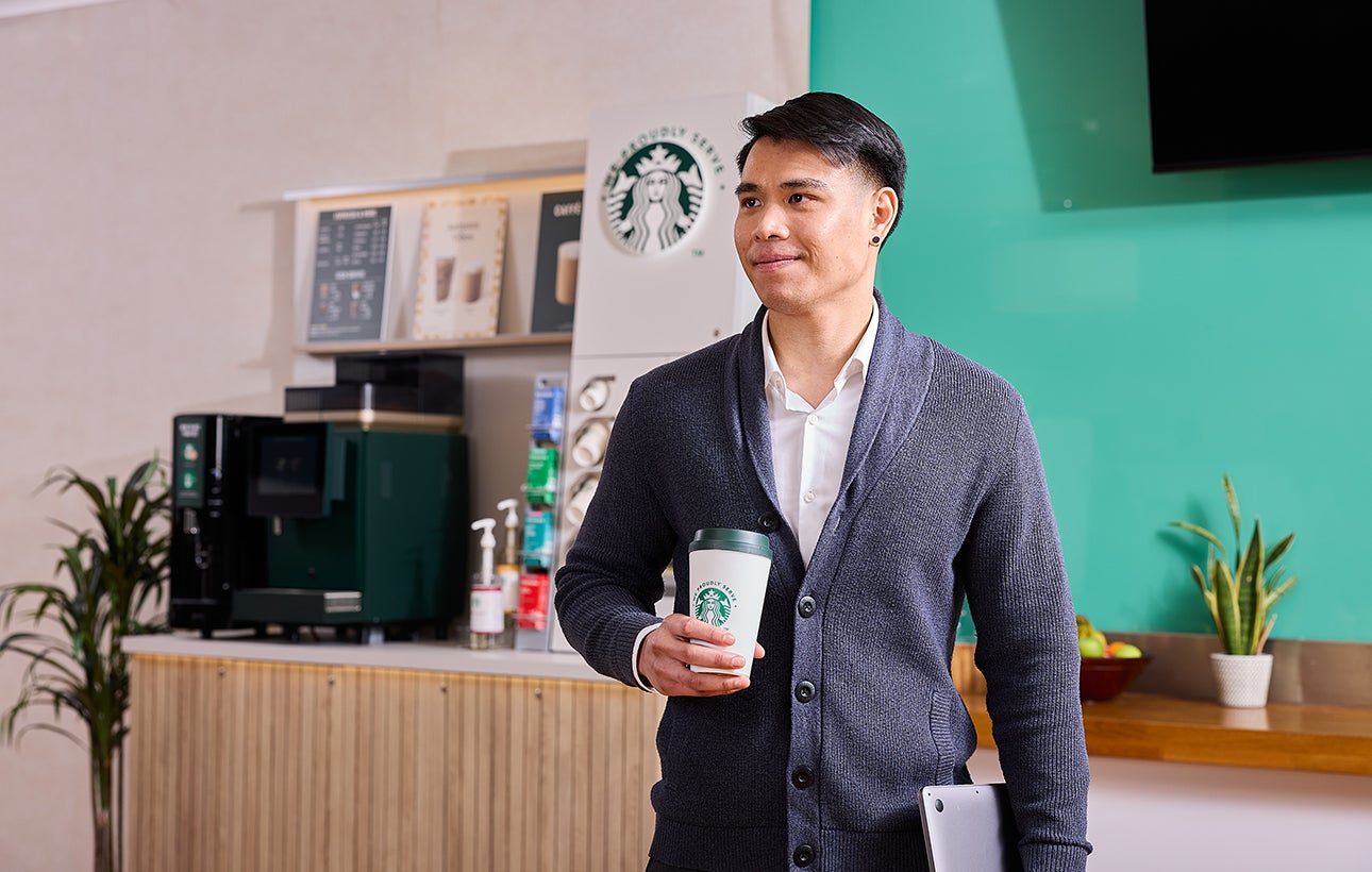 A man holding a We Proudly Serve Starbucks coffee cup
