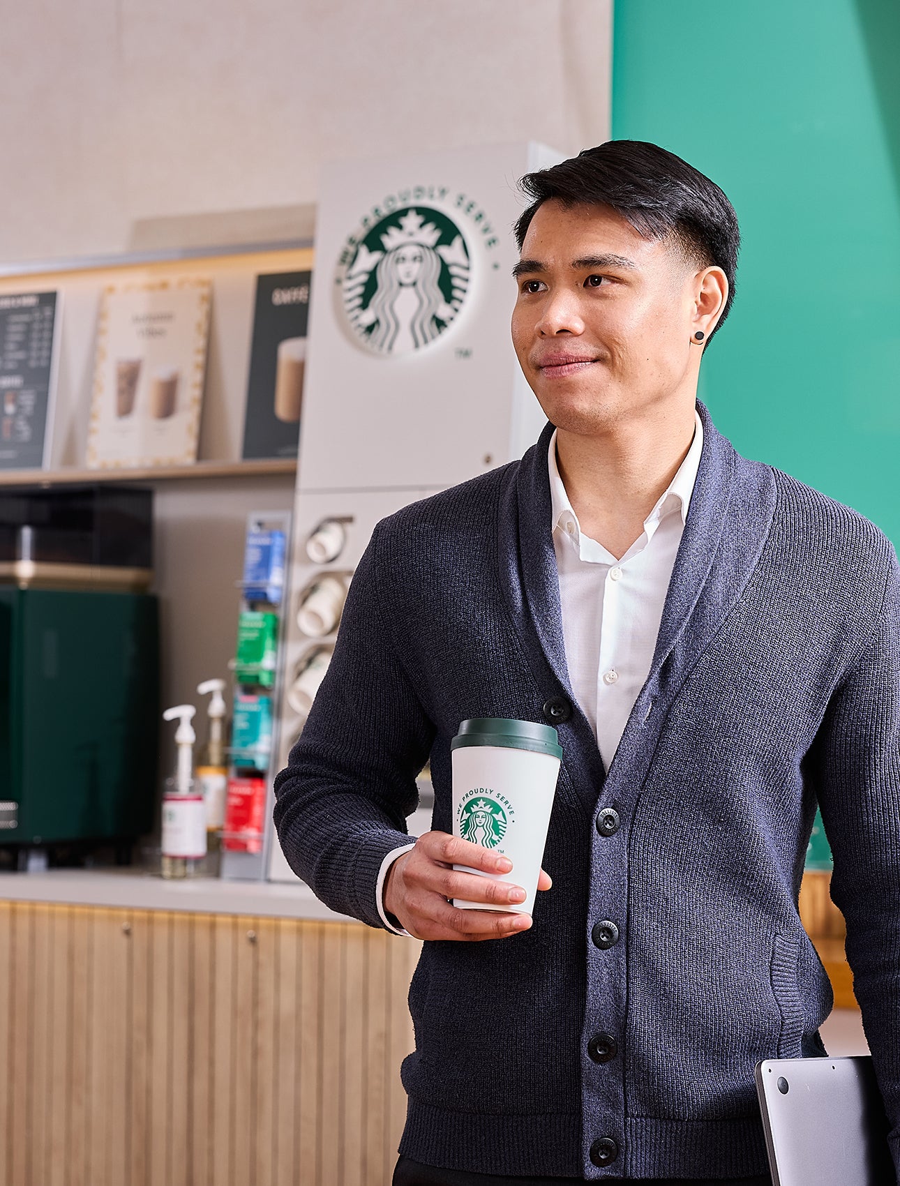 A man holding a We Proudly Serve Starbucks coffee cup