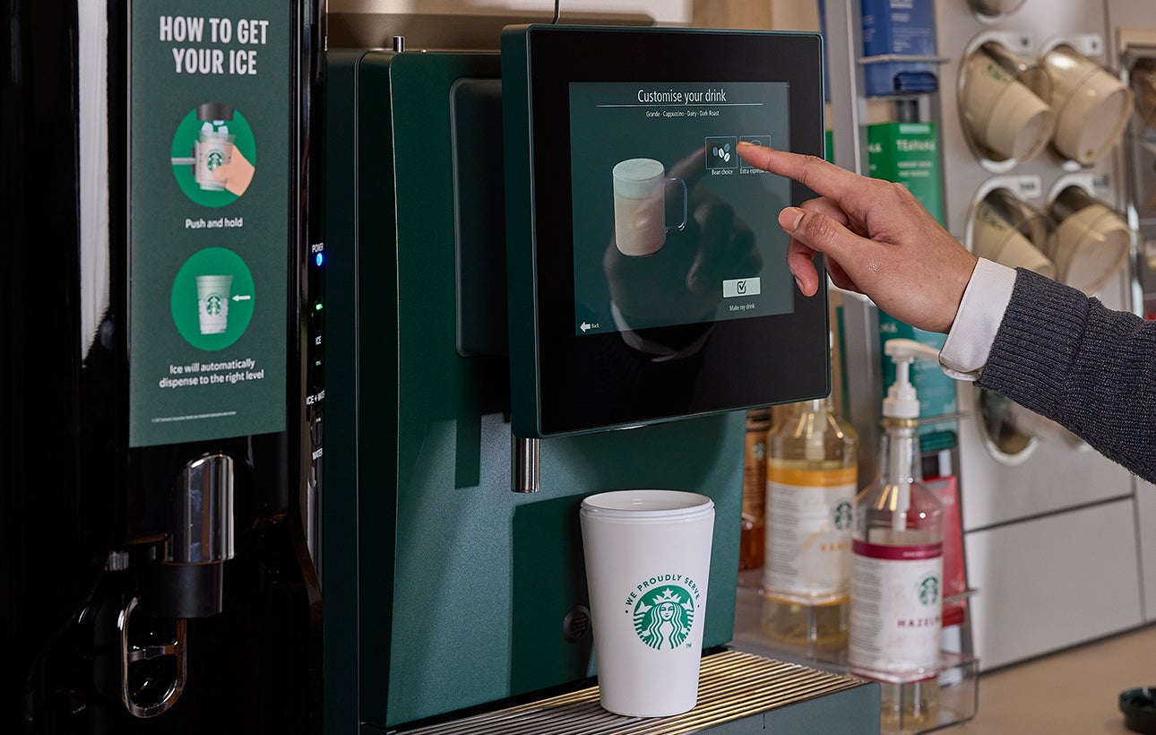 A man selecting a drink on self-serve We Proudly Serve Starbucks coffee machine