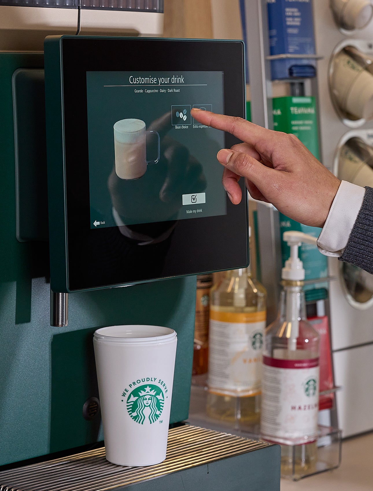A man selecting a drink on self-serve We Proudly Serve Starbucks coffee machine