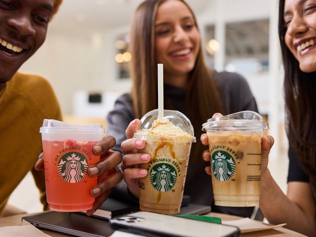Een groep lachende vrienden houdt drie ijskoude Starbucks dranken omhoog