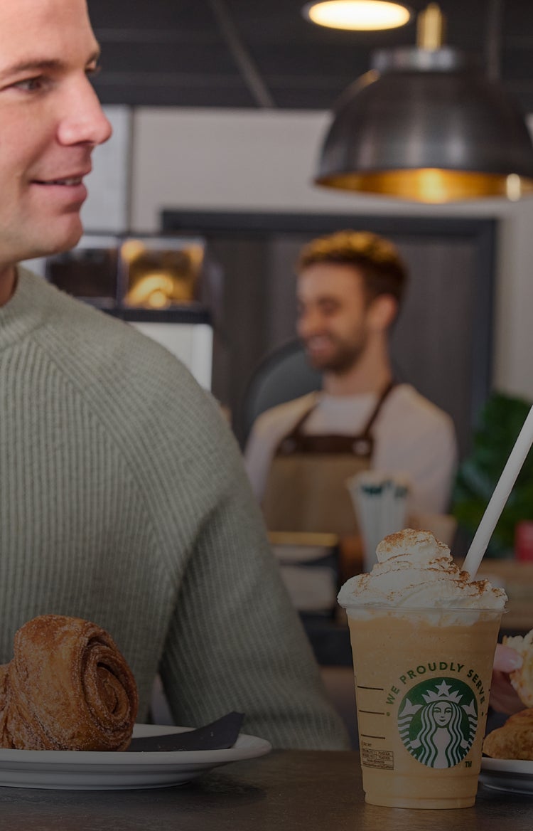 Een man en een vrouw glimlachen naar elkaar in een café terwijl ze genieten van een kop koffie van Starbucks