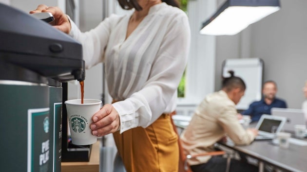ผู้หญิง 1 คนกดกาแฟชงสดจาก We Proudly Serve Starbucks® ในห้องประชุม