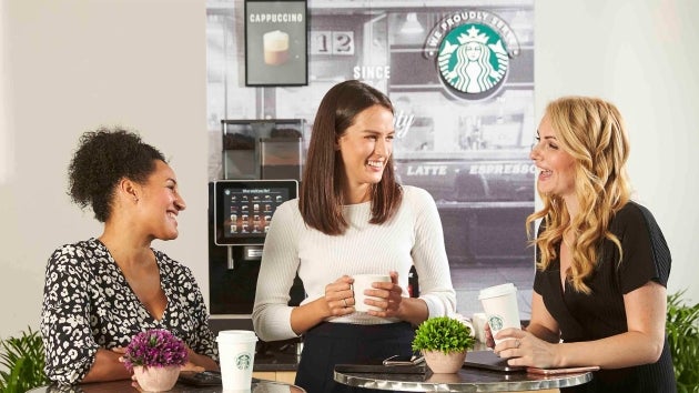 พนักงาน 3 คนกำลังดื่มกาแฟและพูดคุยกันในช่วงพักที่มุมกาแฟของสำนักงาน